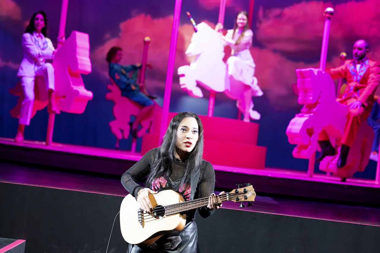 Schwarz gekleidete Frau mit Gitarre singt vor pinkem Karussell