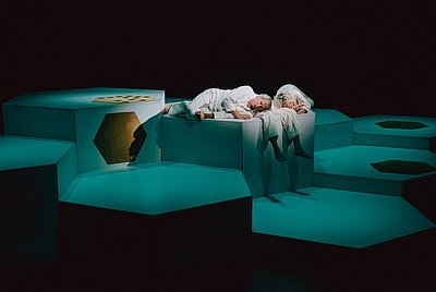 drei Personen liegen auf einem Podest in grünem Licht eingetaucht